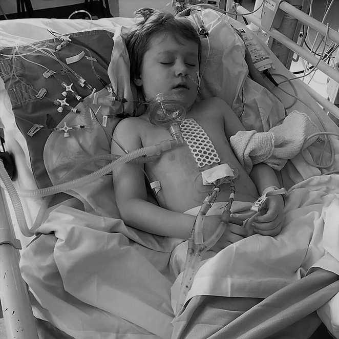 A black and white image of wish child, George lying in his hospital bed, undergoing treatment for his condition.