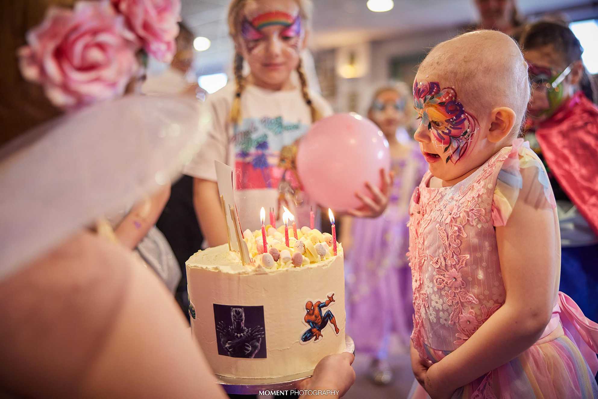 Ryleigh, with her face painted, blowing out the candles on her birthday cake.