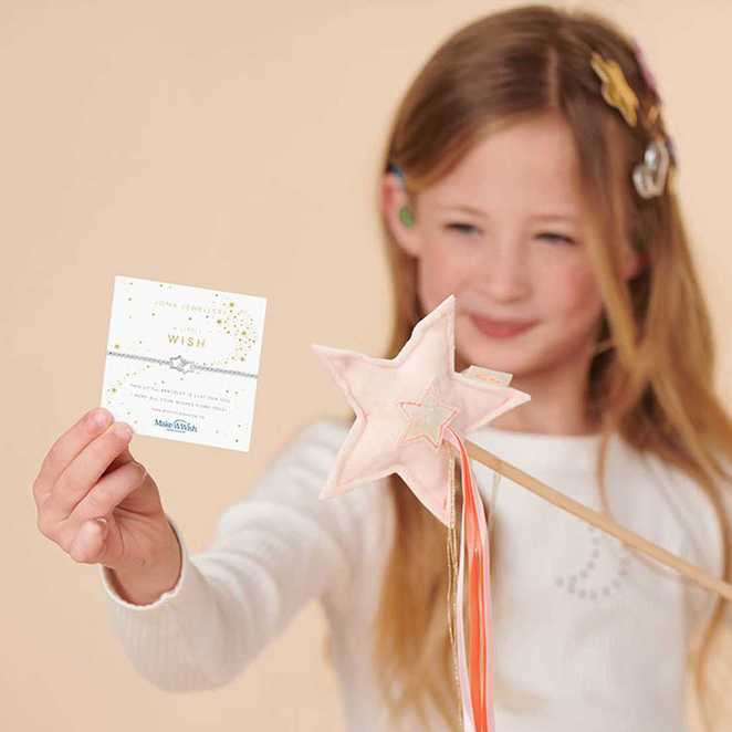 A smiling girl holds a star-shaped wand and a card with small stars.
