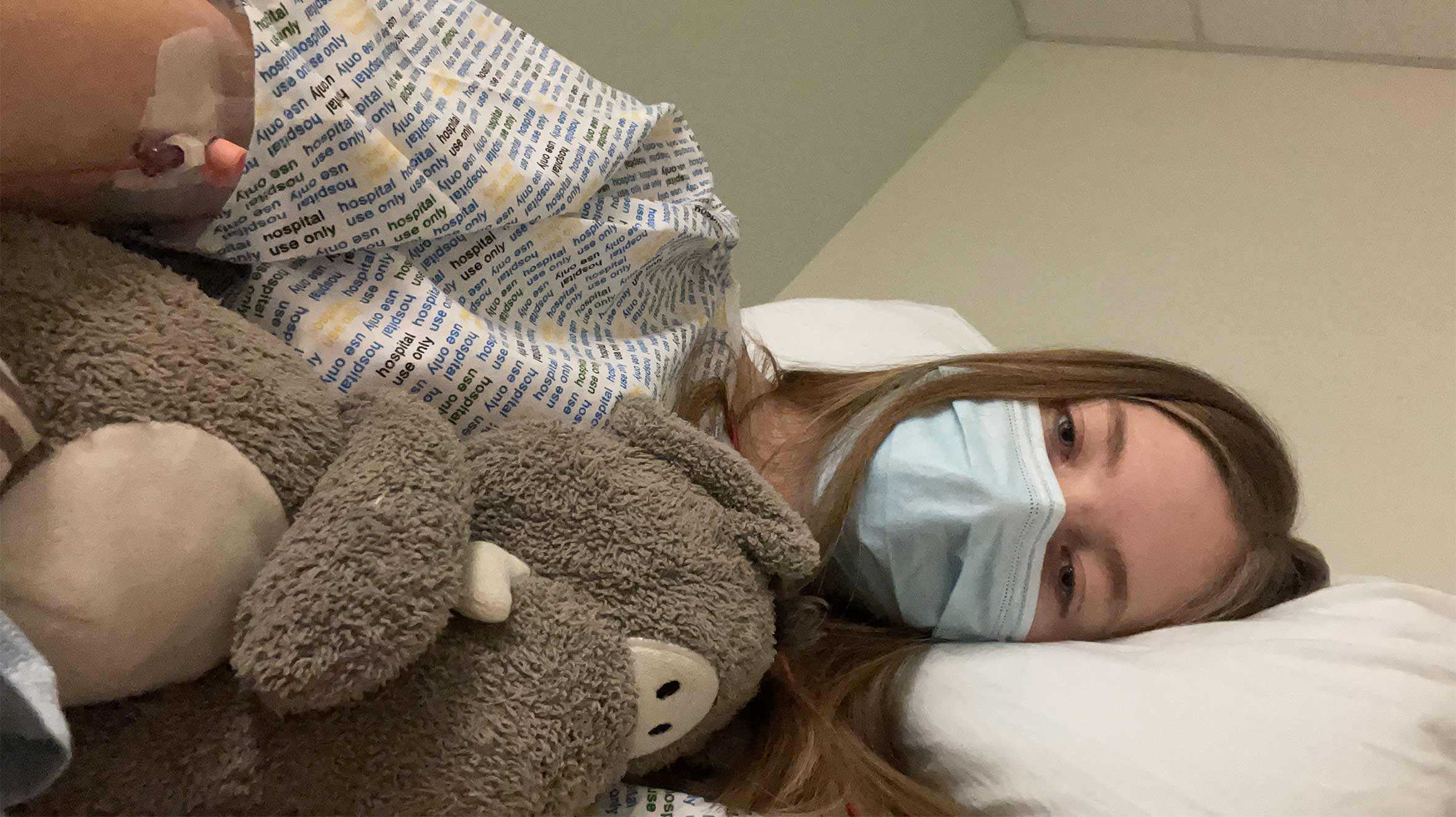 Hayley lying in her hospital bed holding a cuddly toy during treatment for her condition.