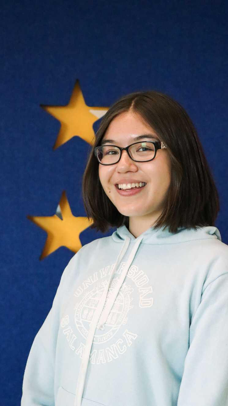 STARboard member Eva is smiling and looking at the camera.  She is wearing glasses and a light blue jumper.