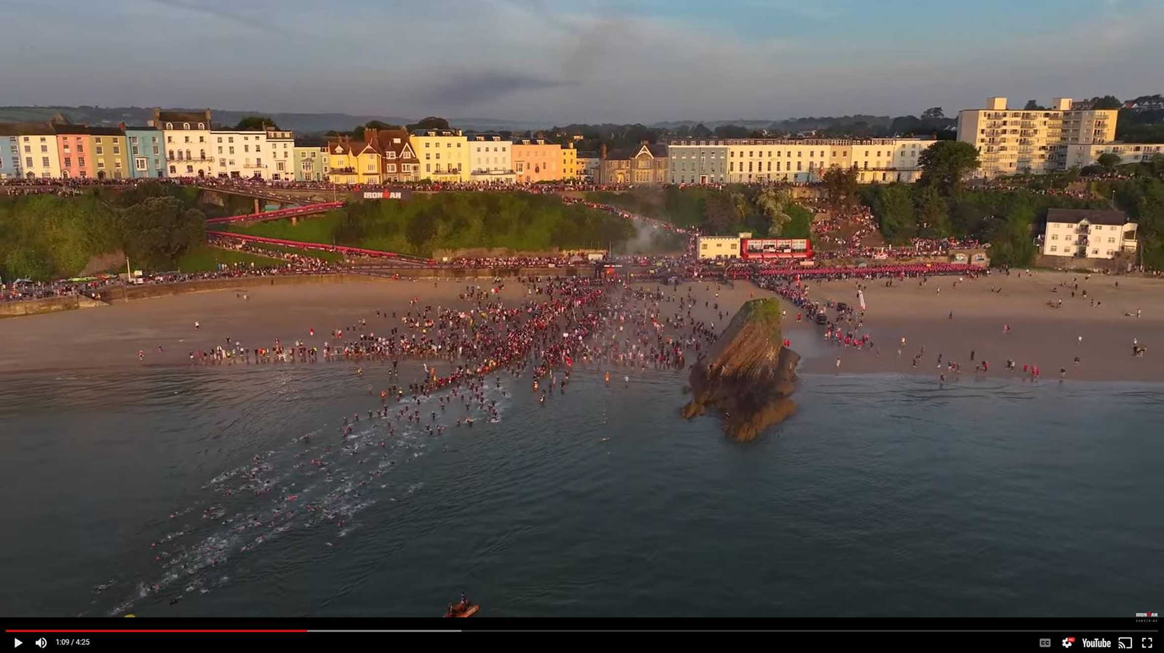 An aerial view of the Wales Ironman course with swimmers entering the water from the beachfront.