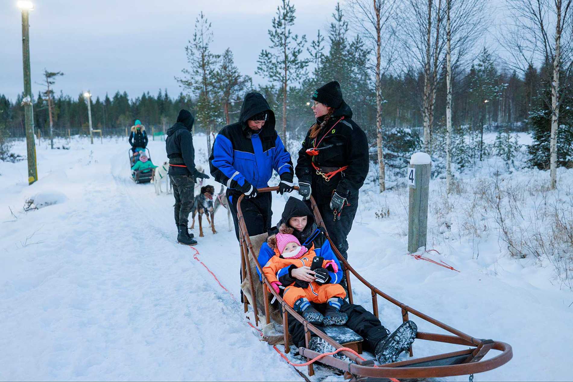 James' dad at the reins of a dog sled with Joshua and Jessie sitting in the sled ready to go.