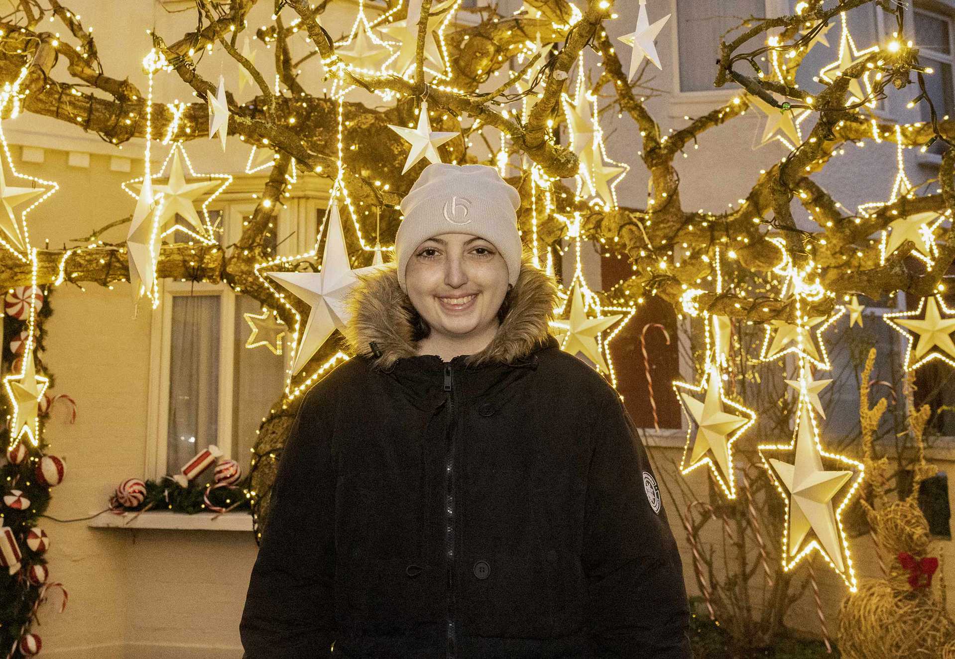 Ellie standing in front of the brightly lit wish tree, outside her house - Image © Phil Harris, Daily Mirror.