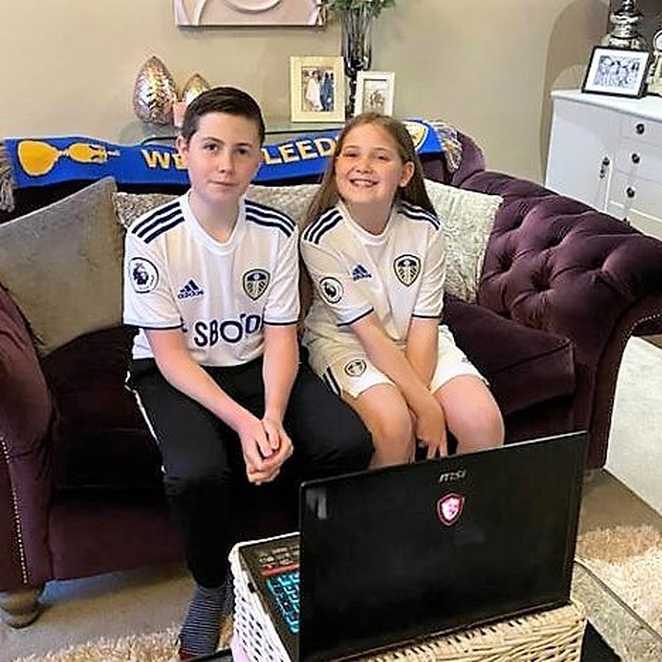 Elliot and his sister, Verity sitting in front of a laptop, wearing their Leeds United kits.