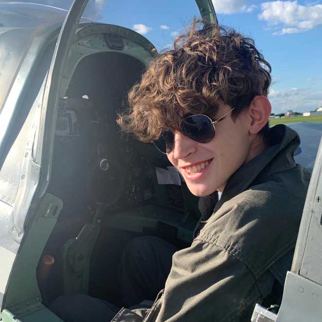 A close up of a smiling Marco sitting in the Sitfire's cockpit in his Aviator sunglasses.
