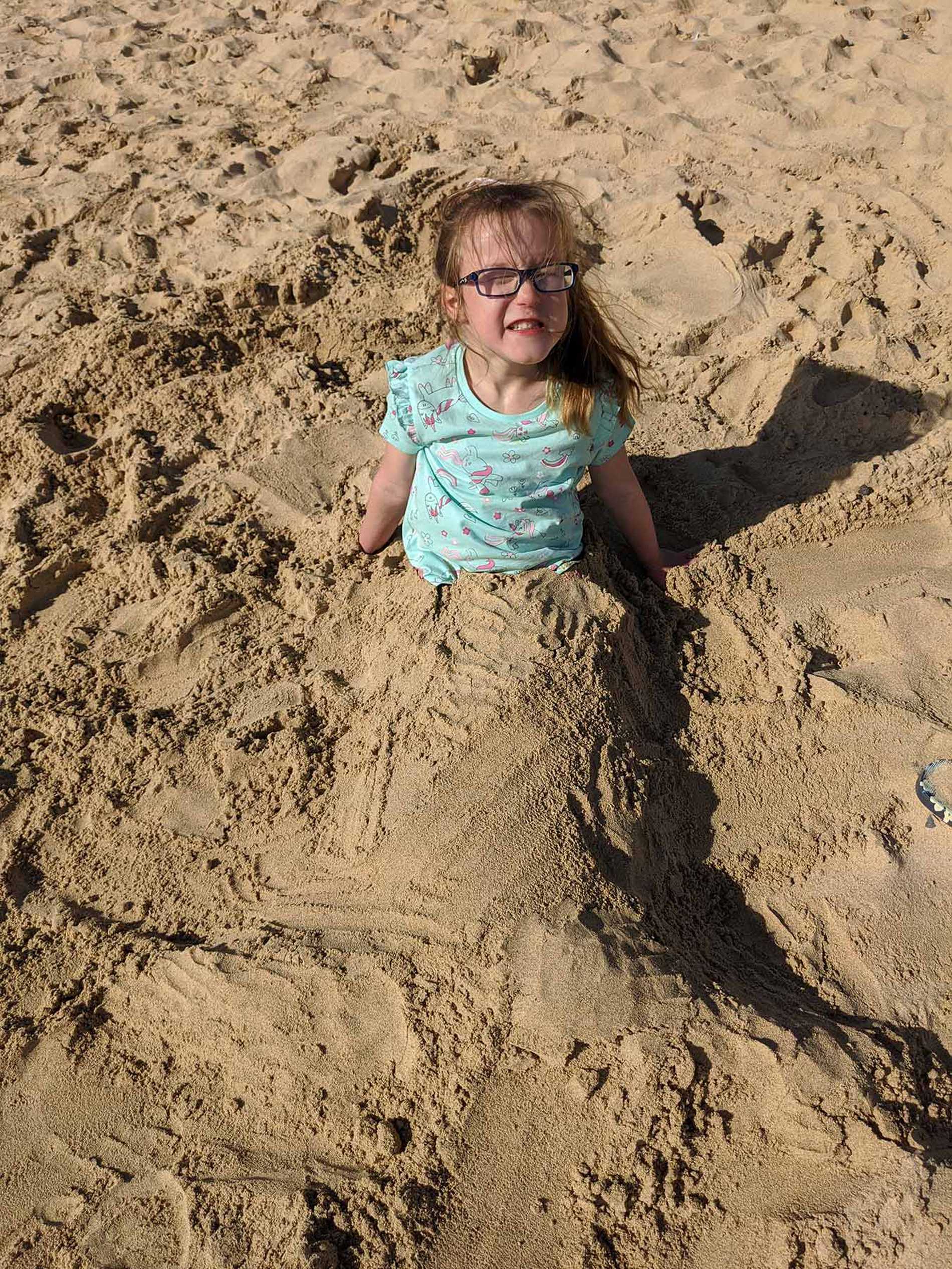 A smiling Hope, on the beach with her legs buried in the sand.