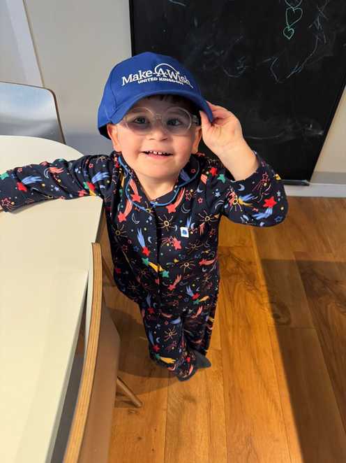 Dzemil is smiling, wearing shooting star pyjamas and wearing a dark blue Make-A-Wish UK hat.