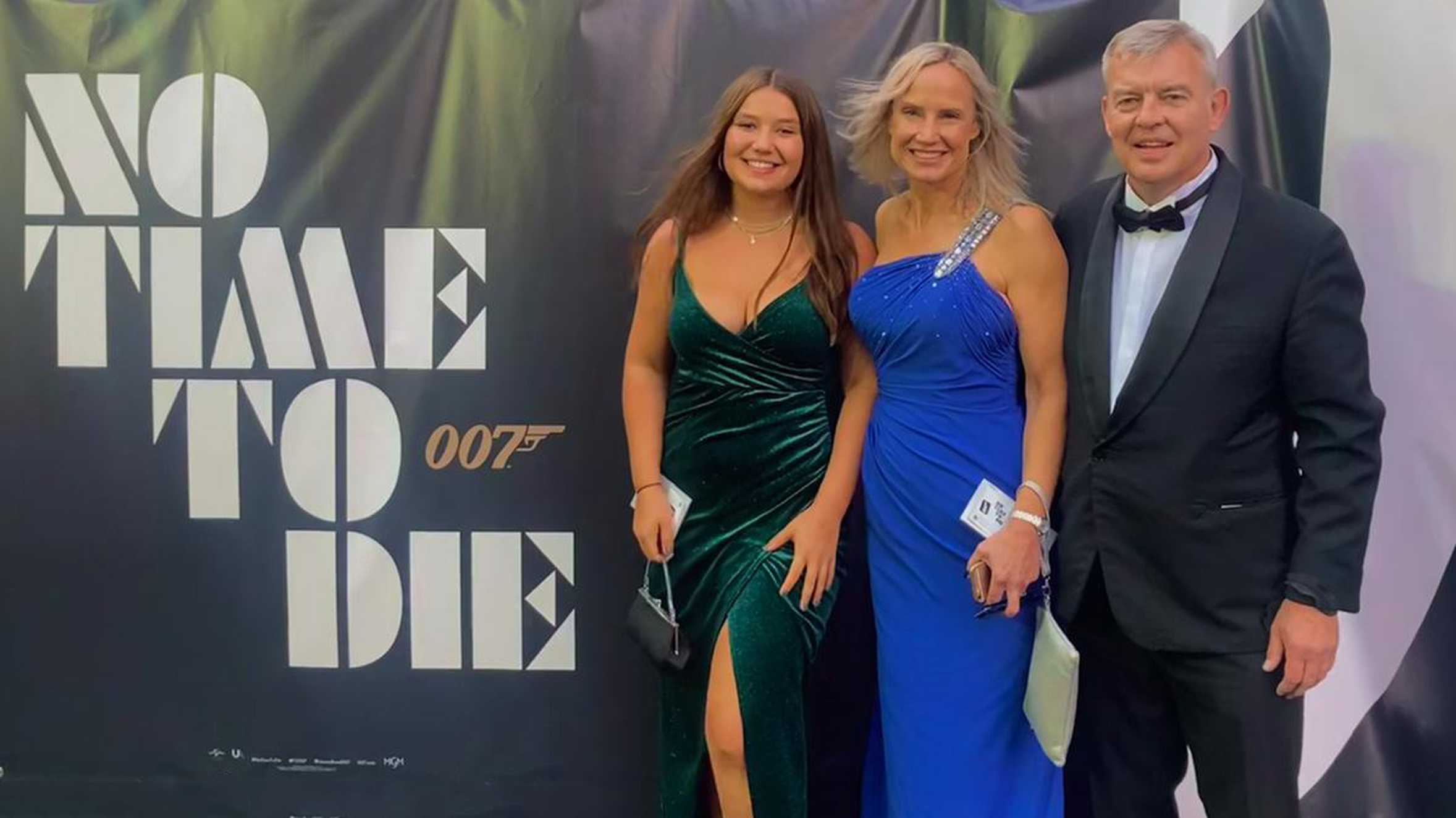 Chloe and her parents posing next to a 'No time to die' banner.