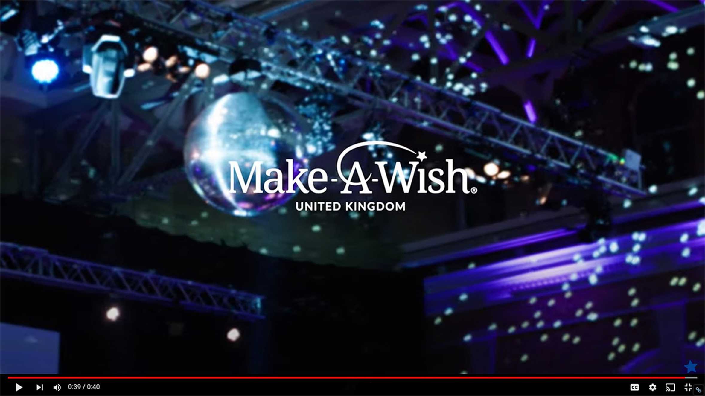 The Make-A-Wish logo in white against a background of the giant glitter ball and lighting gantry from the 2022 Make-A-Wish Ball.