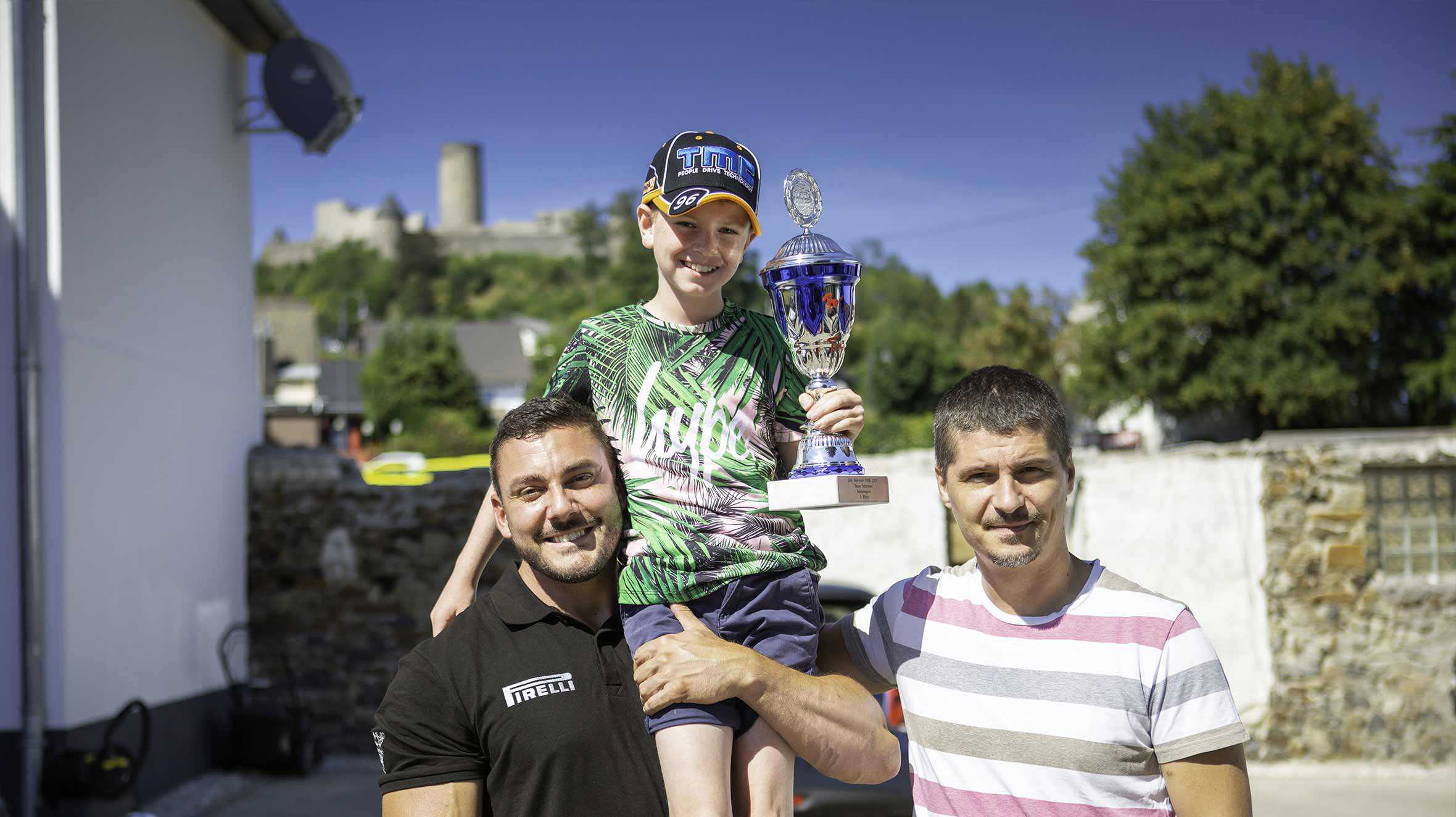 Dewi on the shoulders of a Nuremberg employee and his father, smiing and holding a trophy